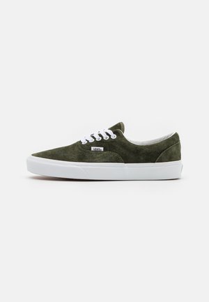 Zapatillas de ante verde con suela de goma blanca. Presenta un diseño clásico de cordones y un cuello acolchado. Etiqueta de logo pequeña en el lado exterior.
