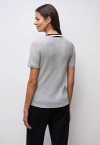 Szary top z krótkim rękawem, o teksturowanym splocie, z czarnym paskiem w kołnierzu i dopasowanym kroju, w połączeniu z czarnymi spodniami.