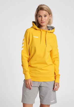 Gelbe Kapuzenjacke mit Kordelzug, langen Ärmeln und weißem Logo. Sie hat ein graues Innenfutter und weiße Chevron-Muster an den Ärmeln.