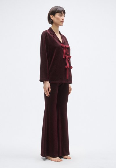 Bourgognefløjls pyjamasæt med en langærmet top med krave og bånddetaljer, kombineret med bukser med vide ben. Blød tekstur og flydende design.