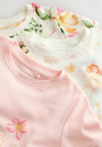 Trzy topy z krótkim rękawem w pastelowych kolorach: jasny róż, oraz wzory kwiatowe na białym tle z różowymi i pomarańczowymi akcentami. Miękka bawełniana tekstura.