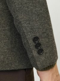 Manche de veste en tissu chevrons gris avec bas de manche tricoté. Détails remarquables : trois boutons noirs sur le bas de manche.
