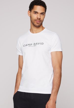 Camiseta de manga corta blanca hecha de algodón con un gran gráfico gris "CAMP DAVID WHITE LABEL" en el frontal. Diseño de corte casual.