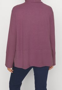 Langärmliges, Rollkragen-Oberteil in einem tiefen Mauve-Ton, aus weichem Stoff gefertigt, mit einem leicht oversized Schnitt und einem abgerundeten Saum.