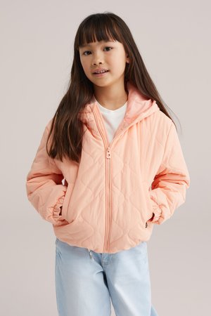 Pihével bélelt, világos rózsaszín kapucnis dzseki; elasztikus mandzsettákkal és elöl cipzáras záródással; világoskék farmerrel párosítva.