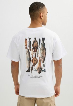 Hombre que lleva una camiseta blanca con ilustraciones detalladas de varias especies de peces y el texto "West Coast Anglers Society" en la espalda.