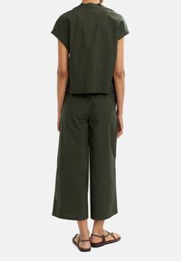 Ciemnozielona, krótka bluzka z krótkimi rękawami w połączeniu z szerokimi spodniami. Materiał ma gładką teksturę i cechuje się luźnym krojem.