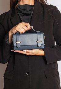 Borsa a tracolla in pelle blu navy con forma rettangolare, doppi manici, dettagli in metallo dorato e una texture liscia.
