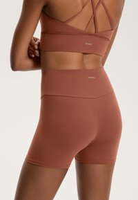 Brun sportbh och shorts set i stretchigt material. Har korslagda axelband och elastisk midja för komfort och stöd.