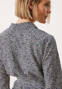 Bluse mit floralem Muster aus navy Stoff, mit Kragen, langen Ärmeln und taillierter Silhouette, die eine dezente Textur und pastellfarbene Akzente aufweist.