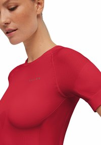Maglietta sportiva rossa con un design aderente, accenti a coste sulle spalle e un sottile logo vicino al collo. Tessuto liscio e maniche corte.