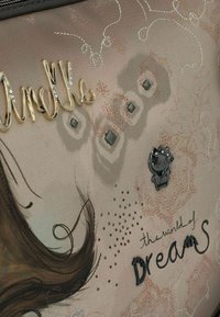 Superficie beige texturizzata con testo decorativo dorato "Anekke", motivi geometrici, un piccolo emblema di gatto e testo in corsivo "il mondo dei SOGNI".