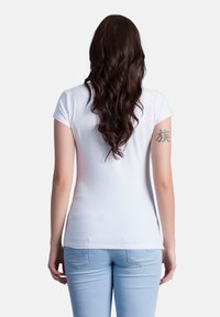 Weißes kurzärmliges T-Shirt mit tailliertem Schnitt, glatter Textur und Rundhalsausschnitt, kombiniert mit hellblauen Jeans.