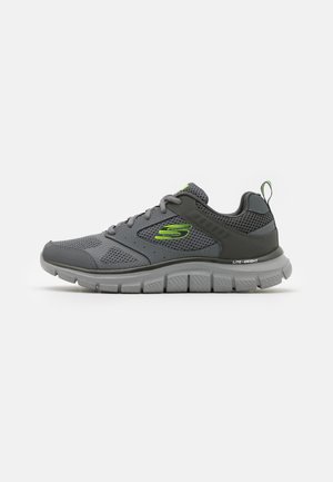 Chaussure de sport grise avec tige en maille, présentant des accents verts. Design léger avec semelle texturée et languette de talon renforcée.
