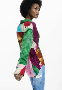 Kleurrijk oversized shirt gemaakt van lichtgewicht stof, met een patchworkontwerp in groen, paars, rood en roze.