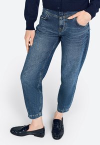 Jeans de mezclilla azul claro con un corte relajado, que presentan una pierna ligeramente ajustada, diseño de cinco bolsillos y dobladillos deshilachados, combinados con mocasines negros.