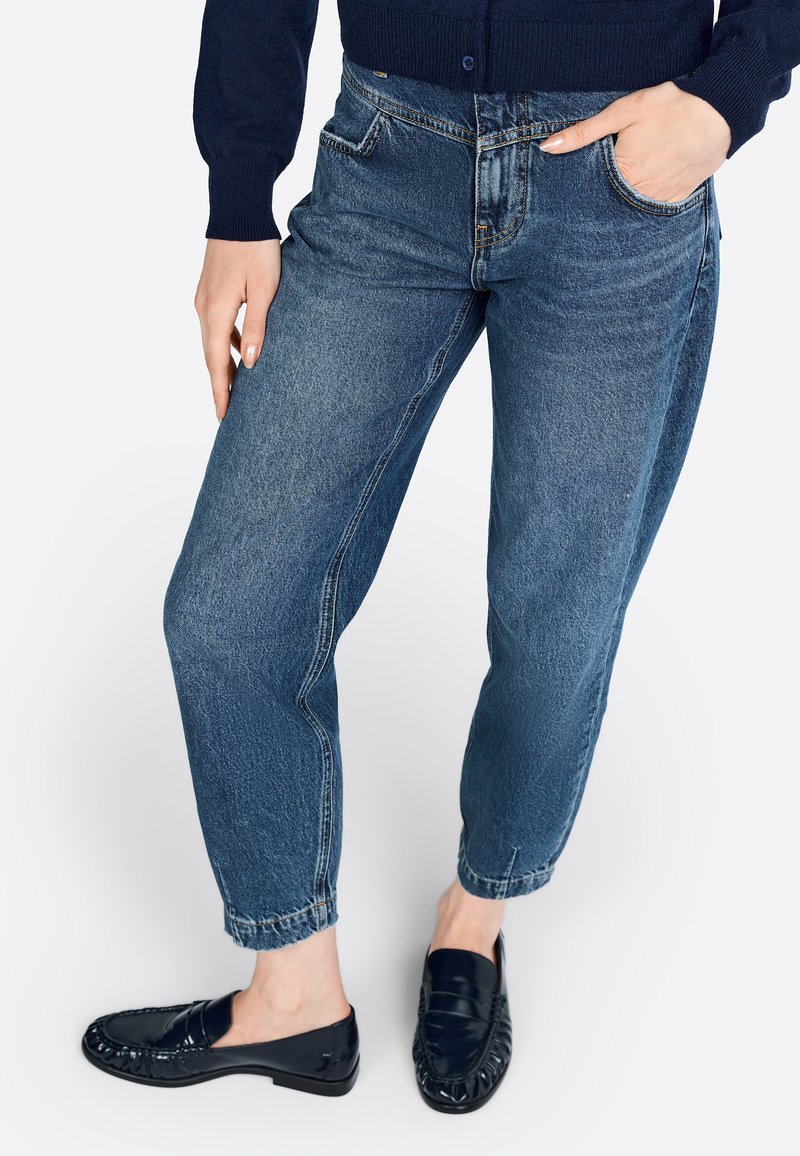 Jeans de mezclilla azul claro con un corte relajado, que presentan una pierna ligeramente ajustada, diseño de cinco bolsillos y dobladillos deshilachados, combinados con mocasines negros.