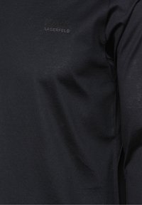 Černý dlouhý rukáv top vyrobený z měkké látky s jemnou strukturou. Má mírný boční rozparek a tónové logo na hrudi.