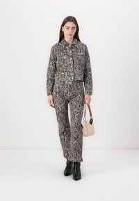 Krokodillemønstret kort jakke og tettsittende bukser i grå nyanser. Modellen holder en beige håndveske. Svarte ankelstøvletter fullfører antrekket.