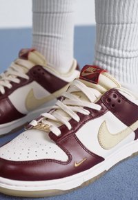 Tenisky Nike Dunk majú bordový kožený zvršok, krémové akcenty, zlaté branding a textúrovanú bielu podrážku. Ľahko perforovaný špička.