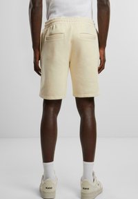 Cream-colored shorts feature an elastic waistband and two back pockets. The fabric appears soft and casual, with a clean, minimal design.