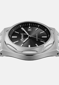 Montre automatique en acier inoxydable avec un cadran noir. Elle possède des index en argent, une fenêtre de date et une lunette ronde lisse.