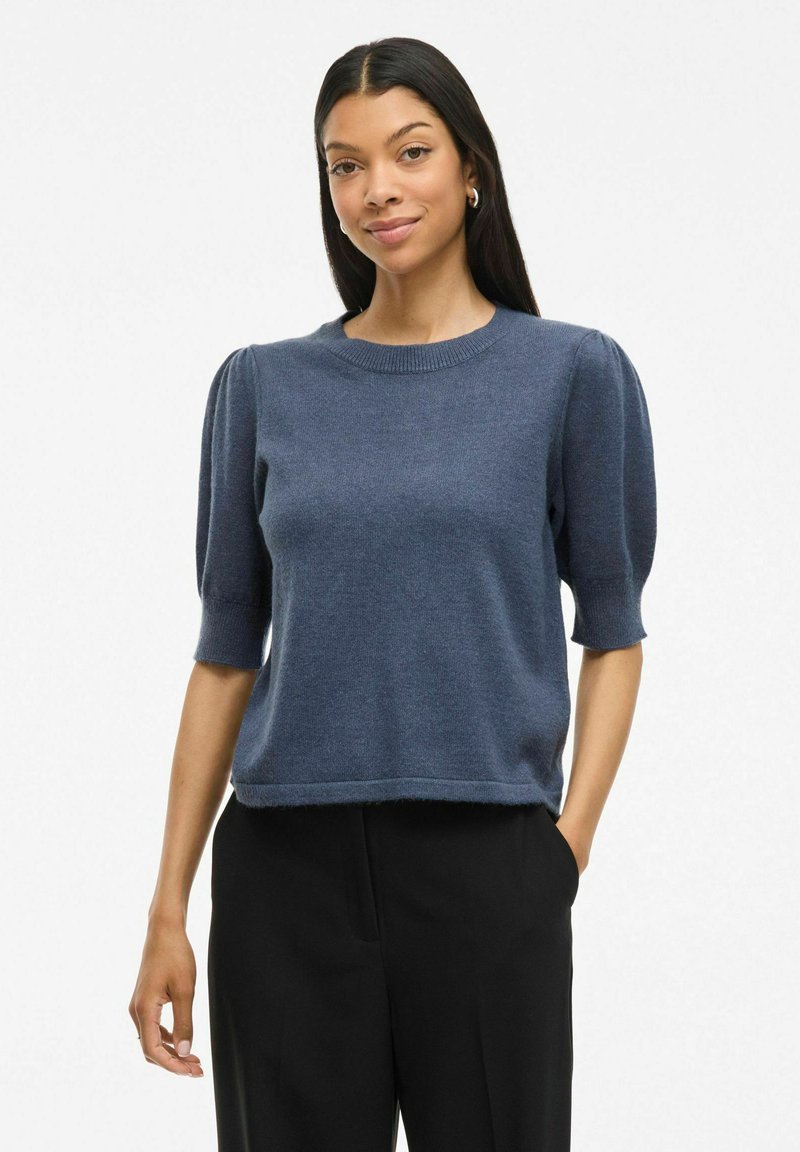 Pull en tricot à manches courtes de couleur bleu foncé, avec un col rond et un design à manches bouffantes, terminé par un ourlet léger.