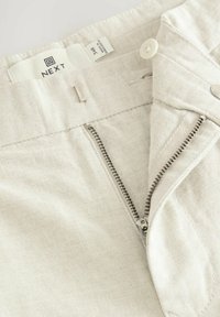 Világos bézs farmernadrág cipzáros, gombos záródással és textil címkével. Az anyag textúrája finom átlós csíkozással rendelkezik.