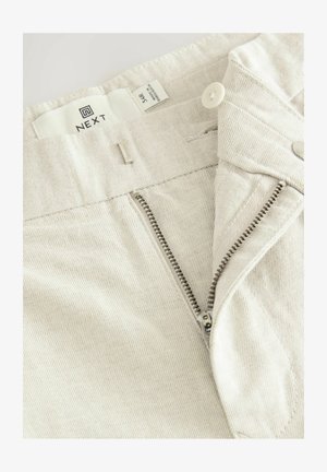 Pantaloni in denim color beige chiaro con zip e chiusura a bottone, e un'etichetta in tessuto. Il tessuto texturizzato presenta un delicato motivo a righe diagonali.