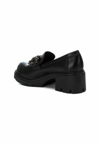 Mocasines de piel negra con una suela gruesa y texturizada y un herraje decorativo en la parte delantera. Punta redondeada y acabado suave.