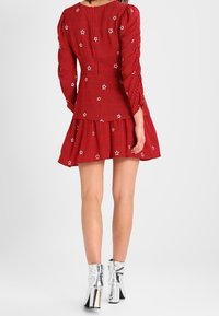 Abito a righe rosse con ricamo di stelle, maniche lunghe e gonna svasata. Abbinato a stivali con tacco argentati lucidi.