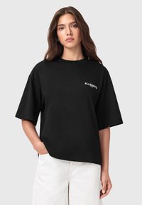 T-shirt in cotone nero oversize con maniche corte e scollo rotondo, caratterizzato da un piccolo logo bianco "ALLSAINTS" sul lato sinistro del petto.