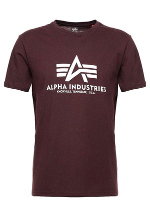 T-shirt en coton marron avec col rond, manches courtes et un logo graphique blanc avec l'inscription "ALPHA INDUSTRIES" et des éléments de design caractéristiques.