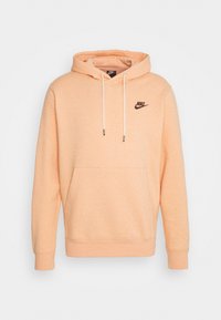 Persikofärgad bomullshoodie med framficka, dragsko i huvudet, ribbade muddar och en liten svart Nike-logga på bröstet.