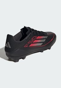 Crampons de football noirs avec des accents rouges, design texturé et silhouette élégante. Dotés d'une tige synthétique et de pointes moulées pour l'adhérence.