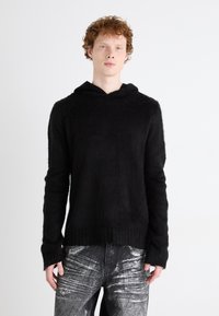 Hoodie preto de malha com um acabamento suave e texturizado. Apresenta uma gola larga e mangas longas com punhos canelados. Combinado com jeans com detalhes em prata.
