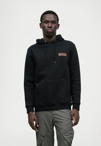 Zwarte hoodie met een voorzak en trekkoorden. Heeft een getextureerde logopatch in rood en wit op het linker borstgedeelte.