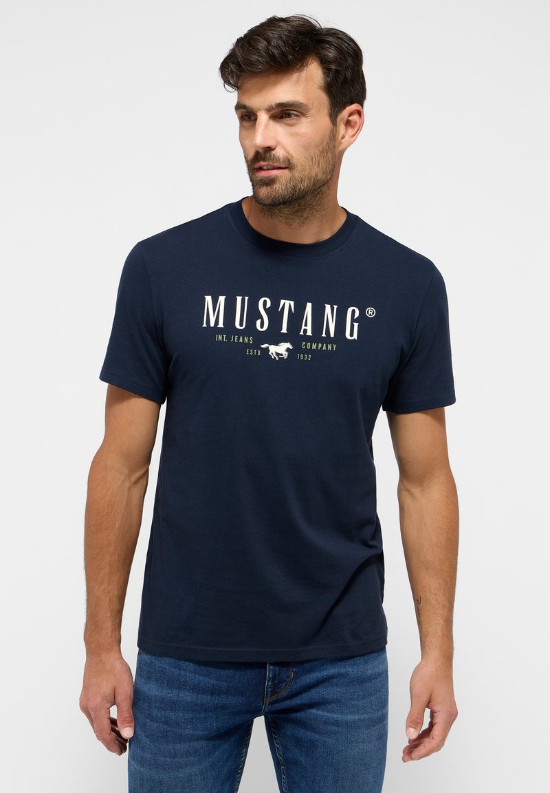 Námořnická modrá bavlněná tričko s bílou a zlatou grafikou "MUSTANG" a datem založení, krátké rukávy a kulatý výstřih.