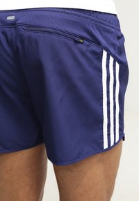 Námořnické sportovní šortky vyrobené z lehké látky, s bílými bočními pruhy a kapsou na zip na zadní straně pro bezpečné uložení.