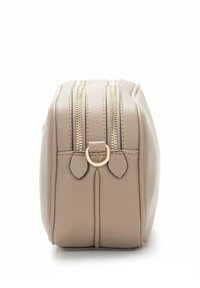 Beżowa prostokątna torba ze skóry z dwoma złotymi suwakami i złotym detalem w kształcie litery D po boku, widoczna z profilu.