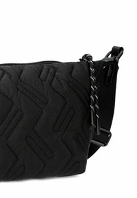Bolso de hombro negro acolchado con patrón de zigzag, cierre con cremallera, correa ajustable y detalle de cordón en blanco y negro en contraste.