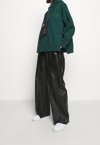 Grön huva sweatshirt med logotyp på framsidan, kombinerad med svarta vida läderbyxor och vita sneakers. Strukturerad tyg och oversized passform.