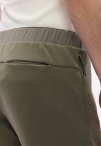 Pehmeästä kankaasta valmistetut oliivinvihreät jogger-housut, joissa on resorivyötärö, vetoketjullinen sivutasku ja sileä pinta.