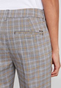 Spodnie w kratę w kolorze szarym, żółtym i czarnym. Posiadają płaski przód, dwie tylne kieszenie oraz gładką teksturę materiału.