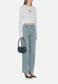 Felpa bianca corta con un ritaglio circolare, abbinata a jeans high-waisted blu chiaro, tacchi a punta neri e una piccola borsa blu.