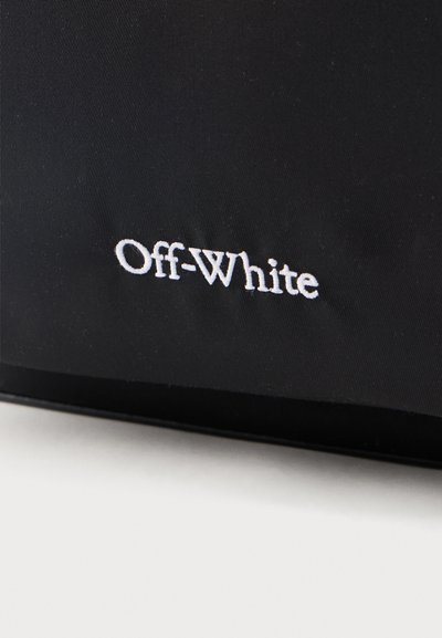 Tissu noir avec "Off-White" brodé en fil blanc, mettant en valeur le logo de la marque sur une surface textile lisse.