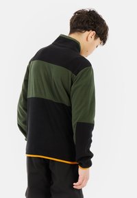 Fleecejack in groen en zwart met hoge kraag, met een kleurgebroken ontwerp en een contrasterende oranje zoom. Zachte textuur en ontspannen pasvorm.