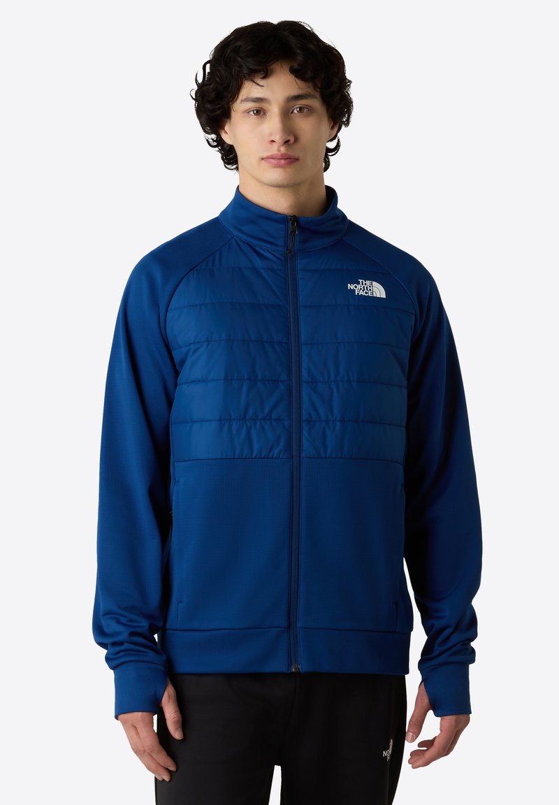 Modrá zipová bunda s polstrovanou přední částí, texturovanými rukávy, stojáčkem a logem na levé hrudi.