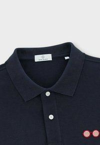 Marineblauwe polo met een gebreide textuur, voorzien van een drie-knopen sluiting en een rood geborduurd brilontwerp op de linkerkant van de borst.