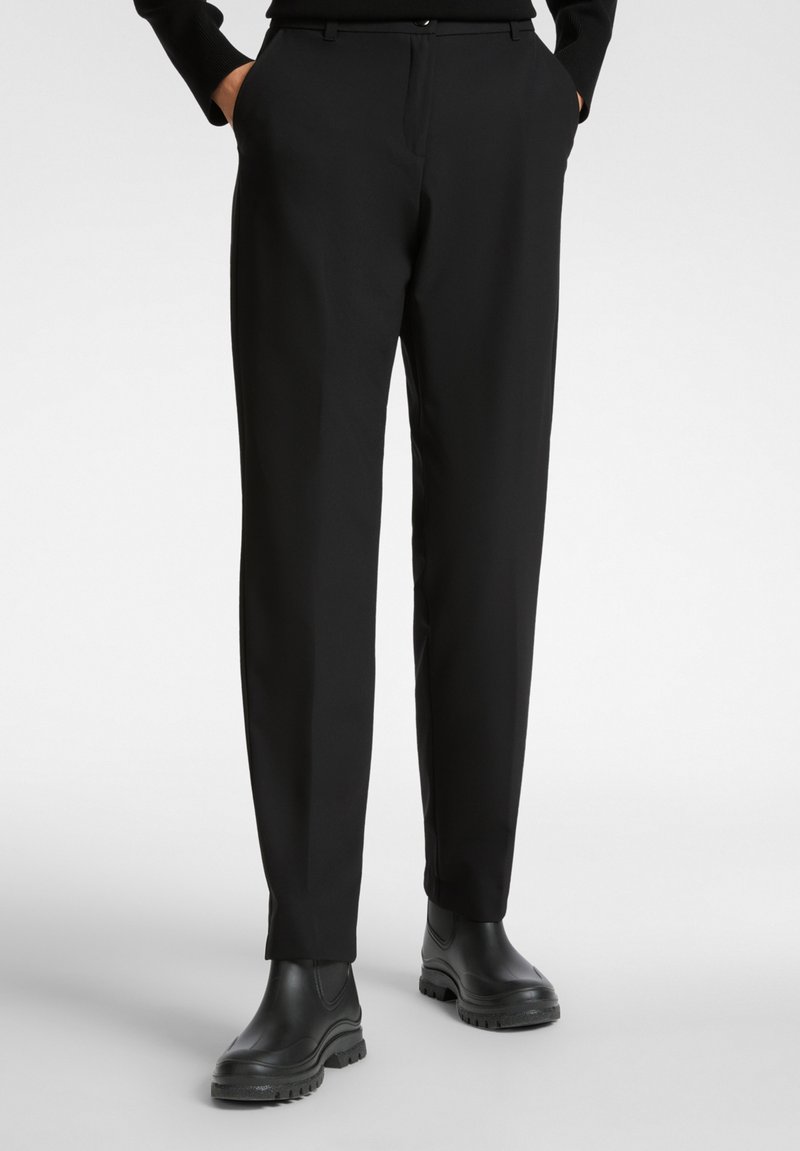 Pantaloni neri realizzati in tessuto liscio, caratterizzati da un taglio classico, tasche laterali e abbinati a stivali neri alla caviglia. Design pulito, senza motivi visibili.